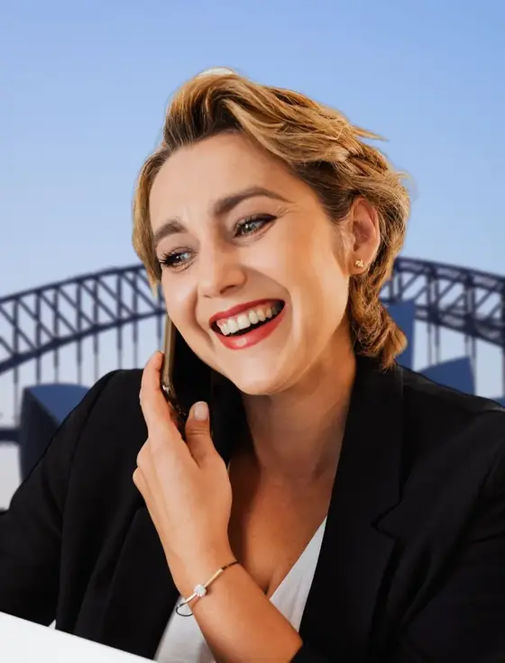 Smiling blonde woman on a phone call in front of the Sydney Harbour Bridge